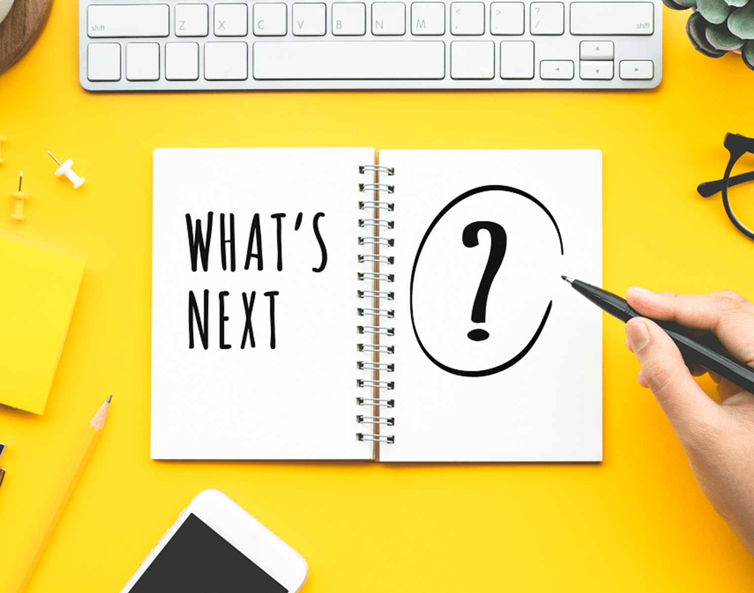A notebook that says 'What's Next' with a large question mark atop a yellow desk. Licensed under Creative Commons.